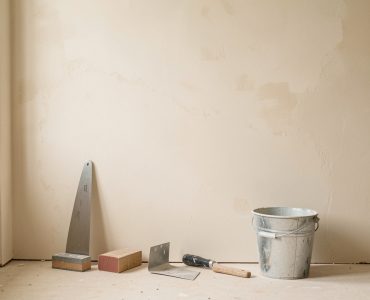Mur intérieur en rénovation avec enduit frais, outils de rebouchage disposés au sol et lumière naturelle douce.