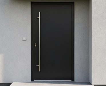 Porte d’entrée noire contemporaine avec poignée en inox sur une façade claire de maison moderne, éclairée par une lumière douce.