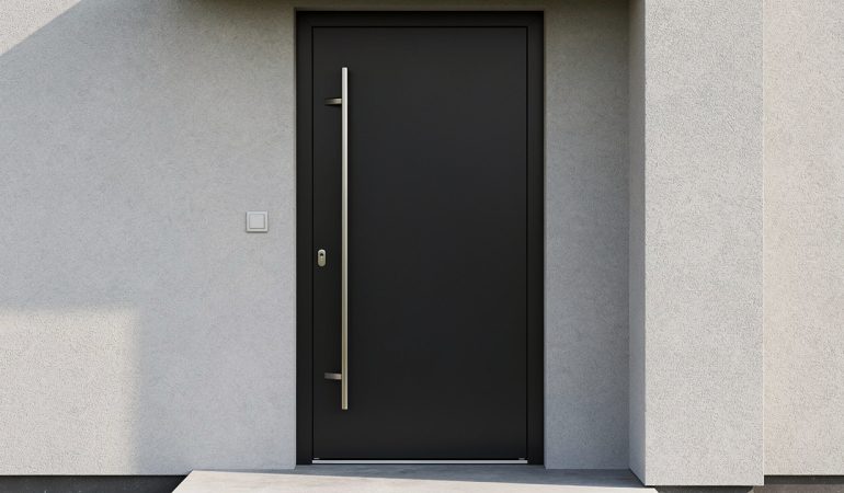 Porte d’entrée noire contemporaine avec poignée en inox sur une façade claire de maison moderne, éclairée par une lumière douce.